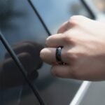 Black Tesery NFC ring worn on a hand beside a Tesla key reader